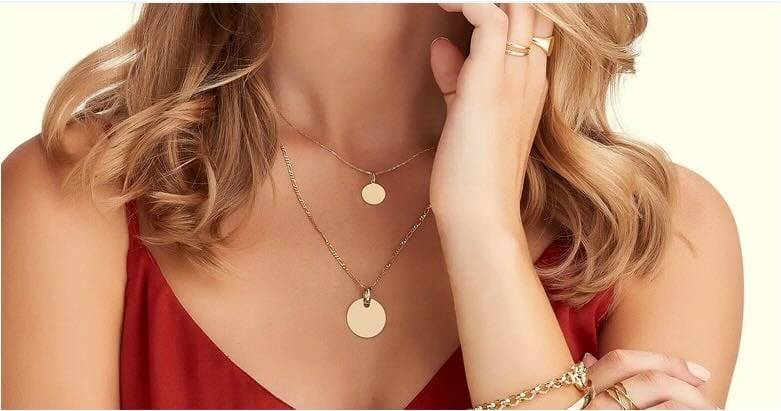 Close-up of a woman's neck and hand showcasing gold layered necklaces, rings, and bracelet.